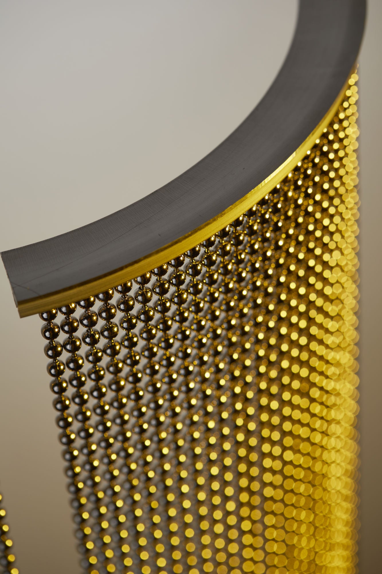 Nickel Plated or Aluminum or silver colored Round metal ball chain hanging vertically on circular track with yellow light shining on the system
